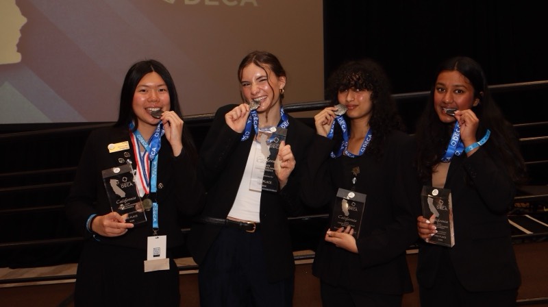 Four Amador Valley DECA members holding their medals and trophies at a conference